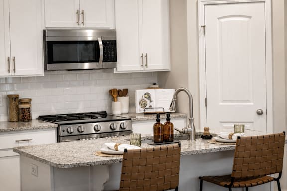 A kitchen with a stove, microwave, and chairs.