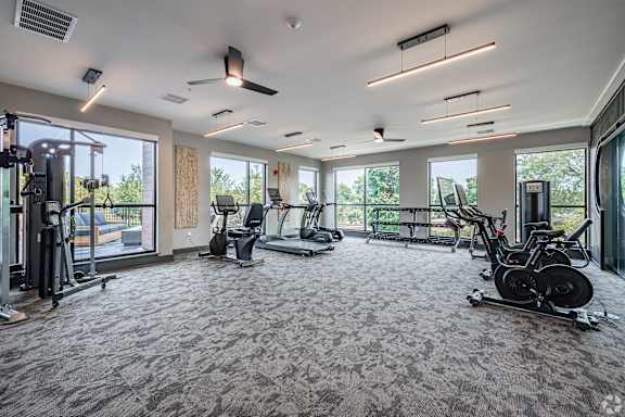 A spacious gym with a variety of exercise equipment and large windows.
