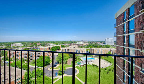 A view from a balcony overlooking a green lawn and a parking lot.