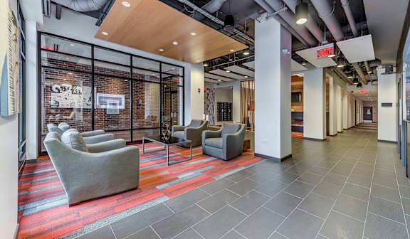 A hallway with grey chairs and a red carpet.