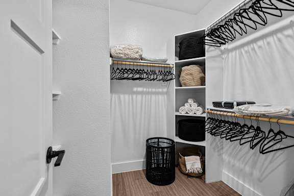 A white closet with black hangers and a black trash can.