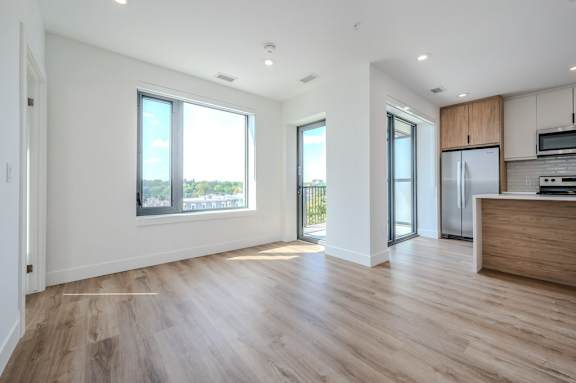 an empty living room with a kitchen and a refrigerator
