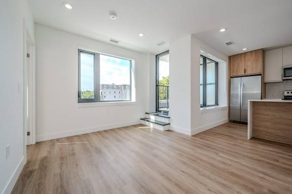 an empty living room with a kitchen and a large window