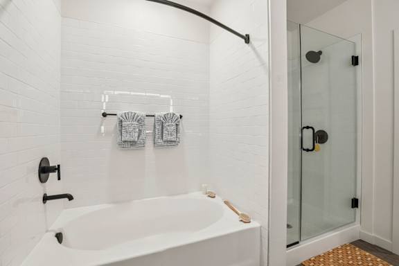 A white bathroom with a white tub and a glass shower door. at Lura Vegas Apartments, Las Vegas, NV, 89103
