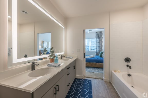 a bathroom with a sink and a tub and a mirror at Aura Vegas Apartments, Las Vegas, NV