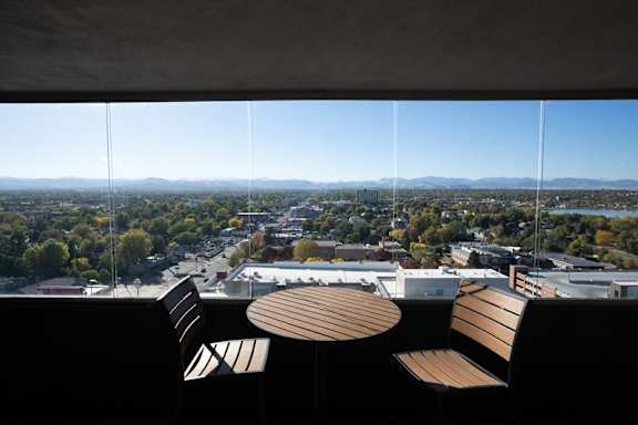 A view of a city from a high vantage point with two chairs and a table in the foreground at Denver Metro Village Apartments, Denver