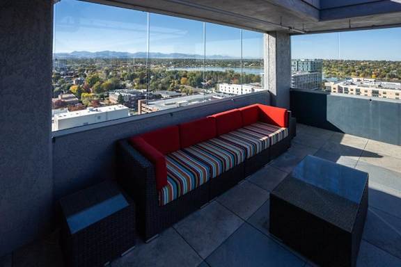 A red and striped couch sits on a balcony with a view of the city at Denver Metro Village Apartments, Colorado