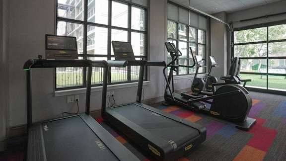 A treadmill and elliptical trainer in a room with large windows at Denver Metro Village Apartments, Denver, CO