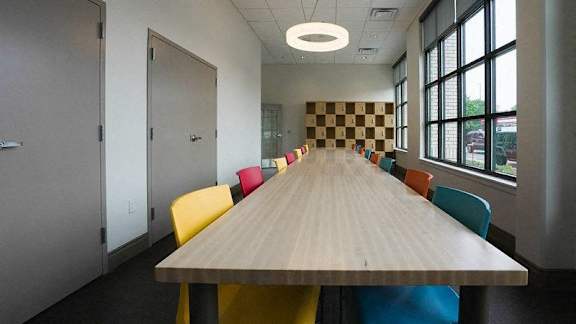 A long wooden table is surrounded by colorful chairs in a room with a checkerboard patterned wall at Denver Metro Village Apartments, Denver
