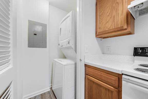A white stackable washer and dryer sits in area next to a kitchen with wooden cabinets at Acclaim at Sterling, in Sterling, VA
