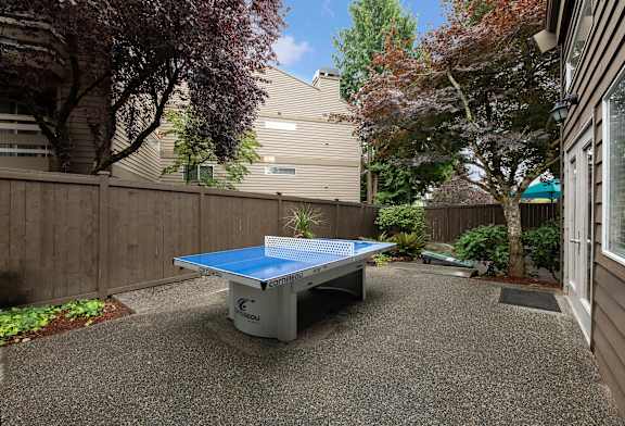 A blue table tennis table is in the middle of a gravel area.