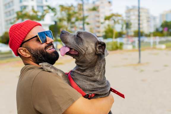 A man in a red beanie and sunglasses is holding a dog on a leash. at City View, Orlando, FL, 32805
