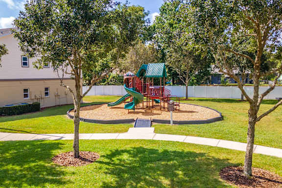 A playground with a green slide and red chairs is surrounded by trees at Academy on Dean Woods Apartments, Orlando, FL, 32825