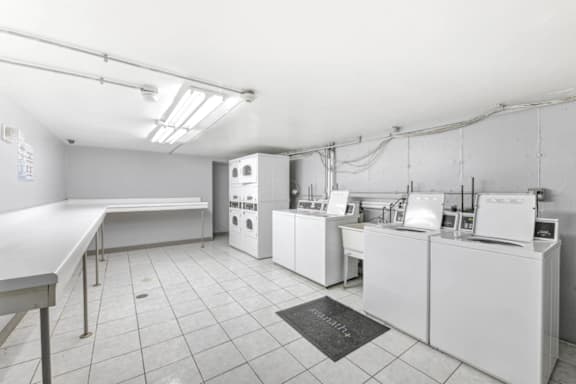A clean, white-walled laundry facilities with multiple washers and dryers with tiled floor