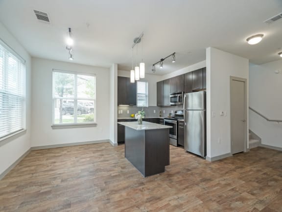 an empty living room with a kitchen with stainless steel appliances
