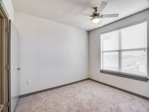an empty bedroom with a large window and a ceiling fan