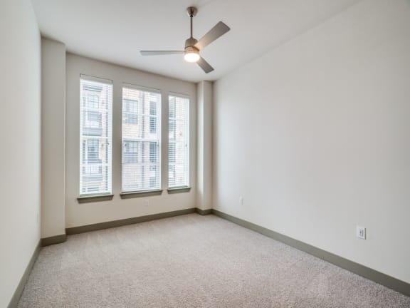 an empty living room with three windows and a ceiling fan
