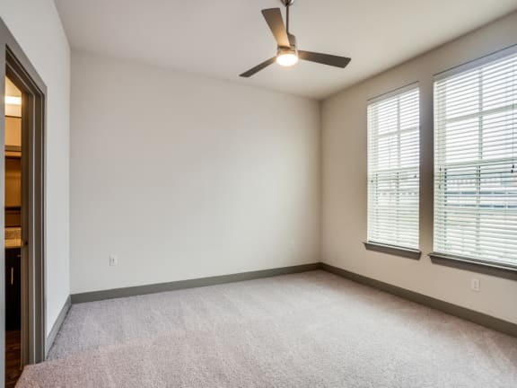 the spacious living room with three windows and a ceiling fan