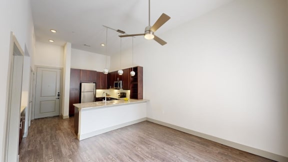 an empty living room with a kitchen and a ceiling fan