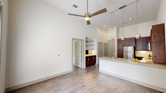 an empty living room with a kitchen and a ceiling fan