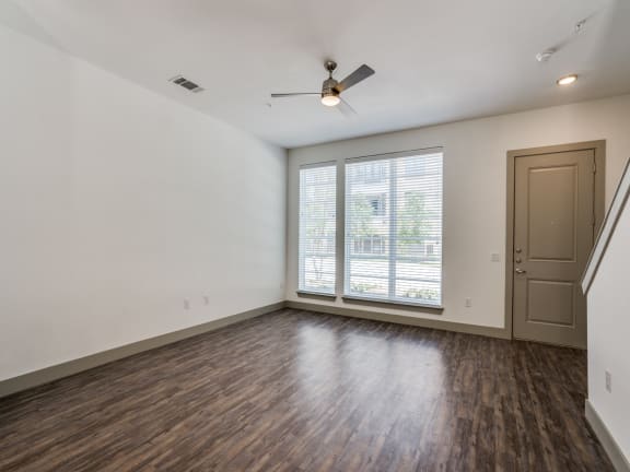 an empty living room with a large window and a ceiling fan