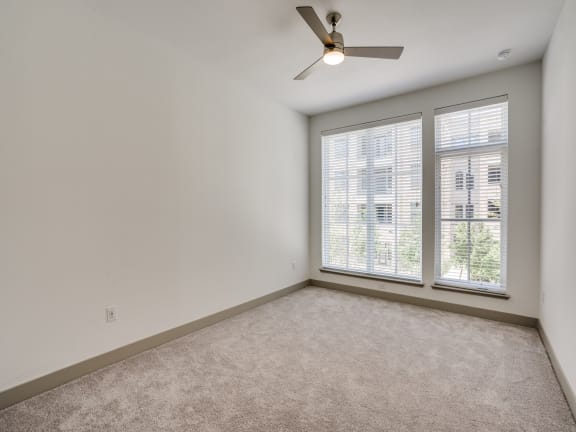 an empty living room with a large window and a ceiling fan