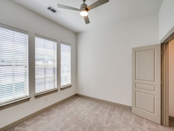 an empty living room with three windows and a ceiling fan
