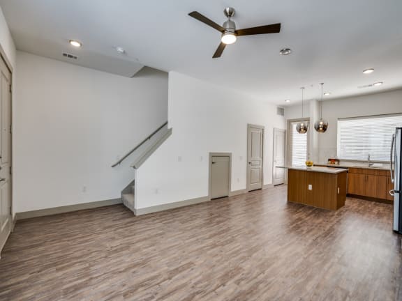 an empty living room with a ceiling fan and a kitchen