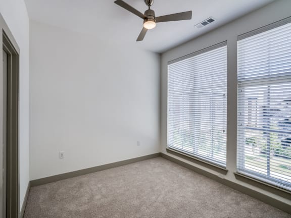 an empty living room with three large windows and a ceiling fan