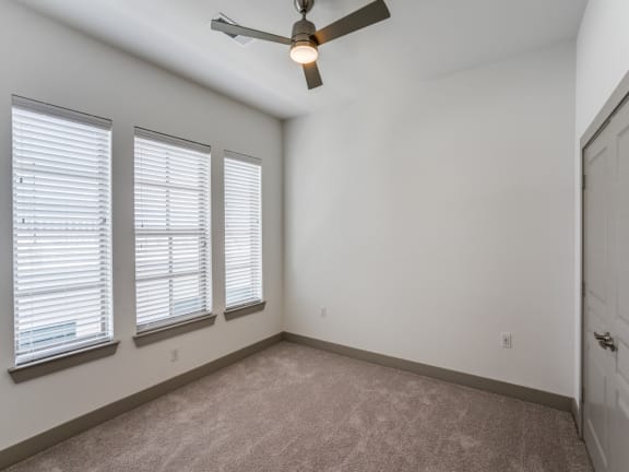 an empty bedroom with a ceiling fan and three windows