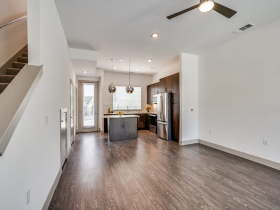 an empty living room with a kitchen and a ceiling fan