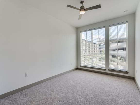an empty living room with large windows and a ceiling fan