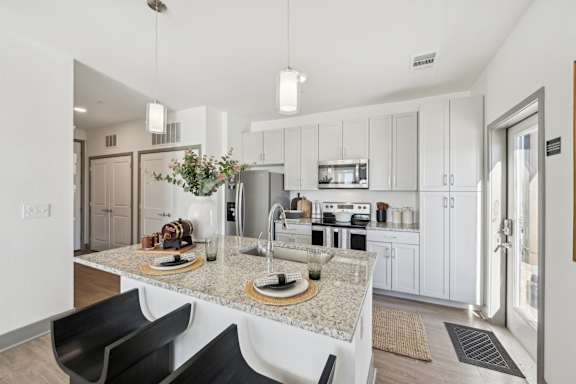 A modern kitchen with a granite countertop and black chairs.