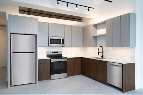 Modern industrial kitchen at Cole Motor Apartments featuring two-tone cabinetry, stainless steel appliances, quartz countertops, matte black fixtures, and contemporary finishes in Indianapolis, IN.