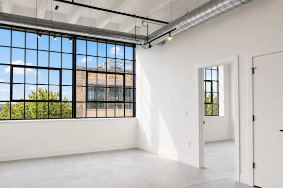 Bright industrial-style apartment at Cole Motor Apartments featuring oversized black-framed windows, polished concrete floors, exposed ductwork, and an open-concept living area in Indianapolis, IN.