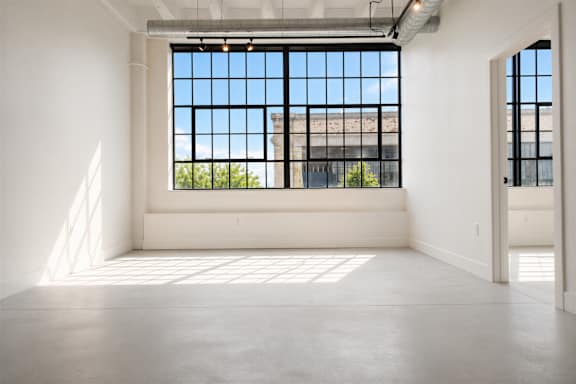 Vacant industrial loft living room at Cole Motor Apartments featuring oversized factory-style windows, polished concrete floors, exposed ceilings, and open-concept apartment design in Indianapolis, IN.