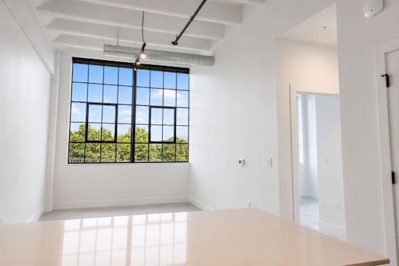 Open-concept apartment interior at Cole Motor Apartments featuring oversized industrial windows, polished concrete floors, exposed beam ceilings, and bright modern finishes in Indianapolis, IN.