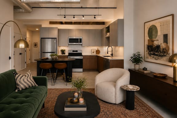 Modern open-concept kitchen and living area at Cole Motor Apartments featuring stainless steel appliances, contemporary cabinetry, industrial-style ceilings, and designer furnishings in Indianapolis, IN.