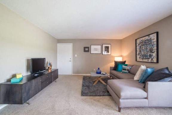 A living room with a grey couch, a wooden entertainment unit, and a rug at Gramercy Apartments, Indiana, 46032