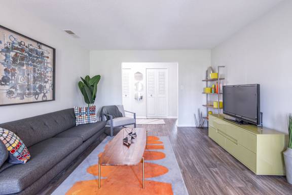A living room with a grey couch, a brown rug, and a yellow cabinet at Gramercy Apartments, Carmel, IN