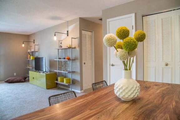 A vase with white flowers sits on a wooden table in a room with a yellow cabinet and shelves at Gramercy Apartments, Carmel Indiana
