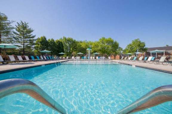 A large outdoor swimming pool with a metal railing in the foreground at Gramercy Apartments, Indiana