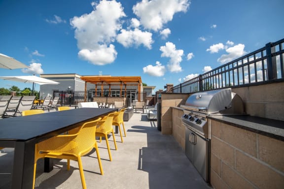 a patio with a grill and tables with yellow chairs at The Century at Purdue Research Park-Student, West Lafayette, IN