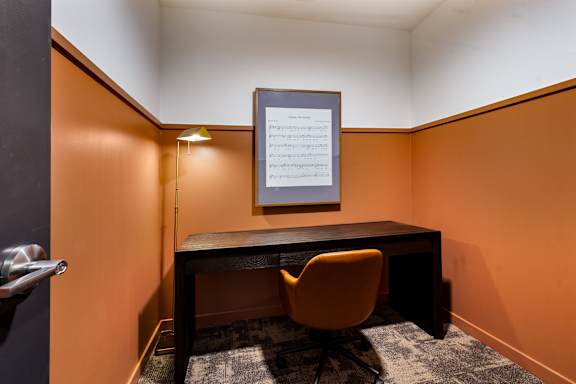 A gold decorated private study room wit desk, chair, lamp, and artwork at The Beverly.