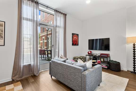 A grey couch in a living room with a television and a window with curtains.
