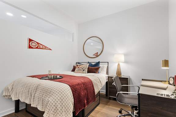 A bedroom with a bed, desk, chair, and lamp.