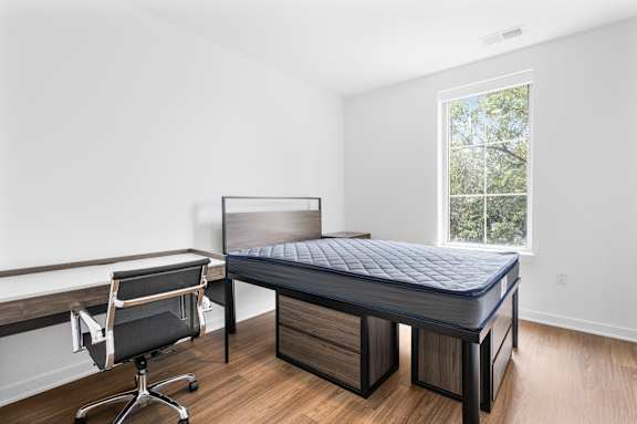 A bedroom with a bed, chair, and window.