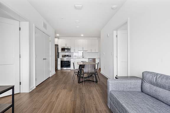 A modern kitchen with white cabinets and a grey sofa.