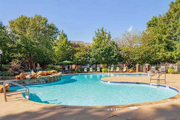 Resort-style swimming pool with waterfall feature, lush landscaping, and lounge seating at Village at Almand Creek apartments in Conyers, GA. Ideal for relaxation and outdoor enjoyment.