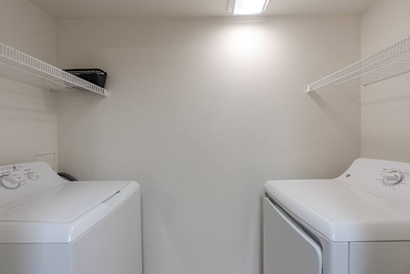 Two white front load washing machines in a small laundry room at FALLS CREEK APARTMENTS, Coeur DAlene
